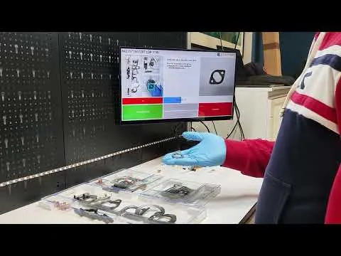 Operator in gloves at a lit workstation following on-screen assembly instructions